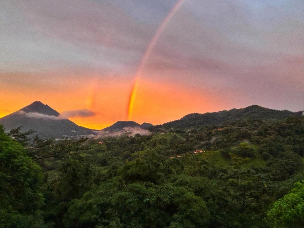 a rainbow in the sky over a forest with mountains at AsiaTica Lodge Volcano and Lake View in El Castillo de La Fortuna