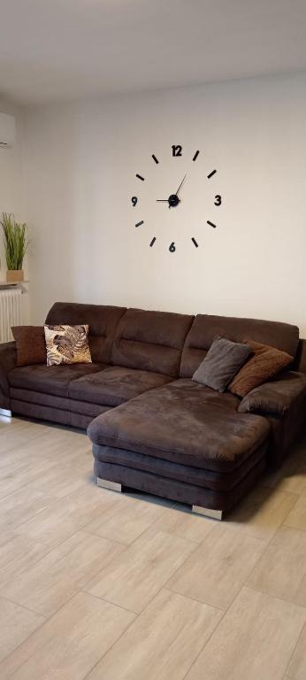 a brown couch in a living room with a clock on the wall at Appartamento Malignani in Cervignano del Friuli