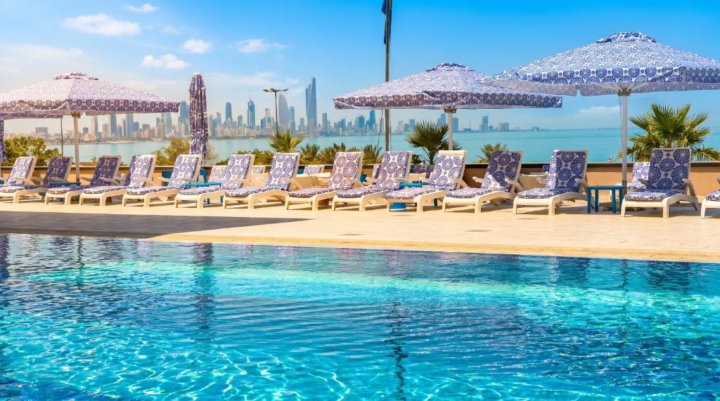 a row of chairs and umbrellas next to a swimming pool at Symphony Style Hotel Kuwait in Kuwait