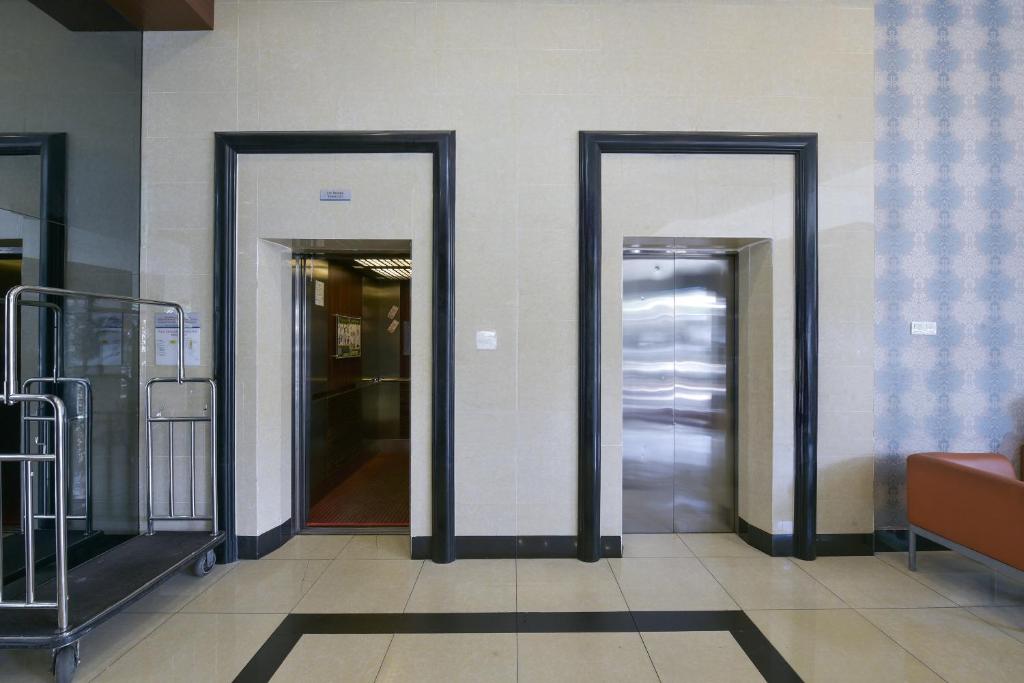Two open elevator entrances sit beside a luggage trolley in a tiled lobby.