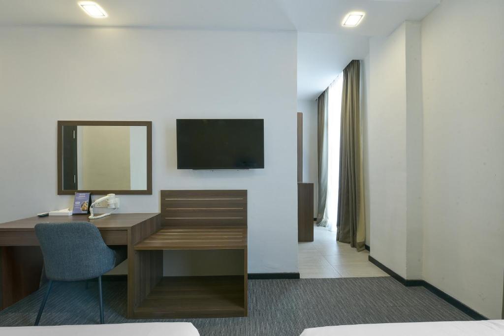 A furnished room corner with a writing desk, mirror, TV console and curtained window.
