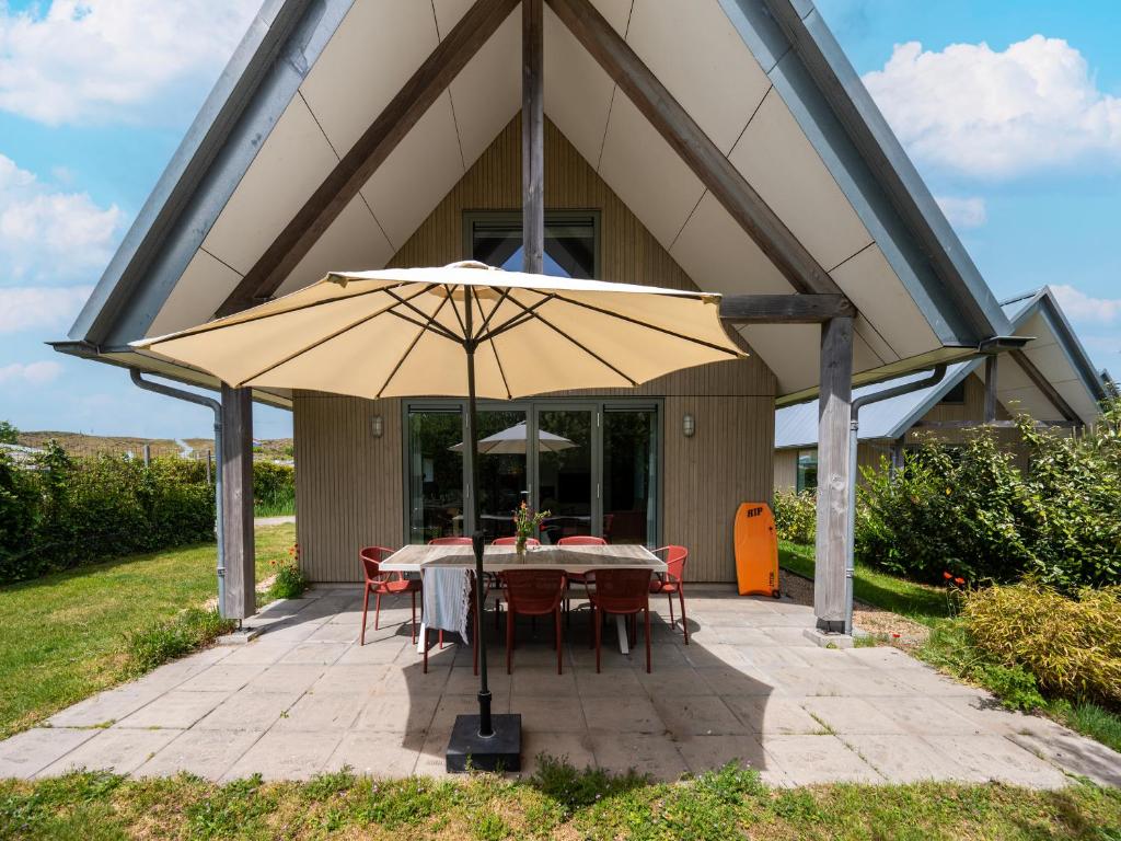 a table and chairs under an umbrella on a patio at Aan Noordzee Villa Veranda huisdier toegestaan max 2 in Sint Maartensvlotbrug