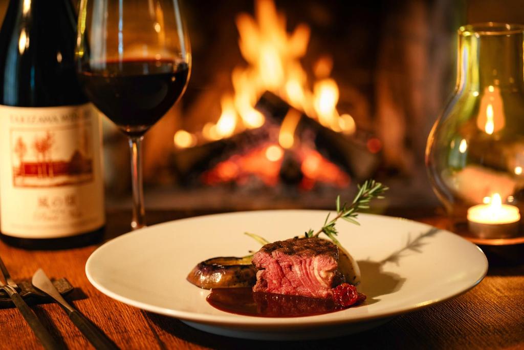 a plate of food on a table with a glass of wine at Log Hotel The Maple Lodge in Iwamizawa