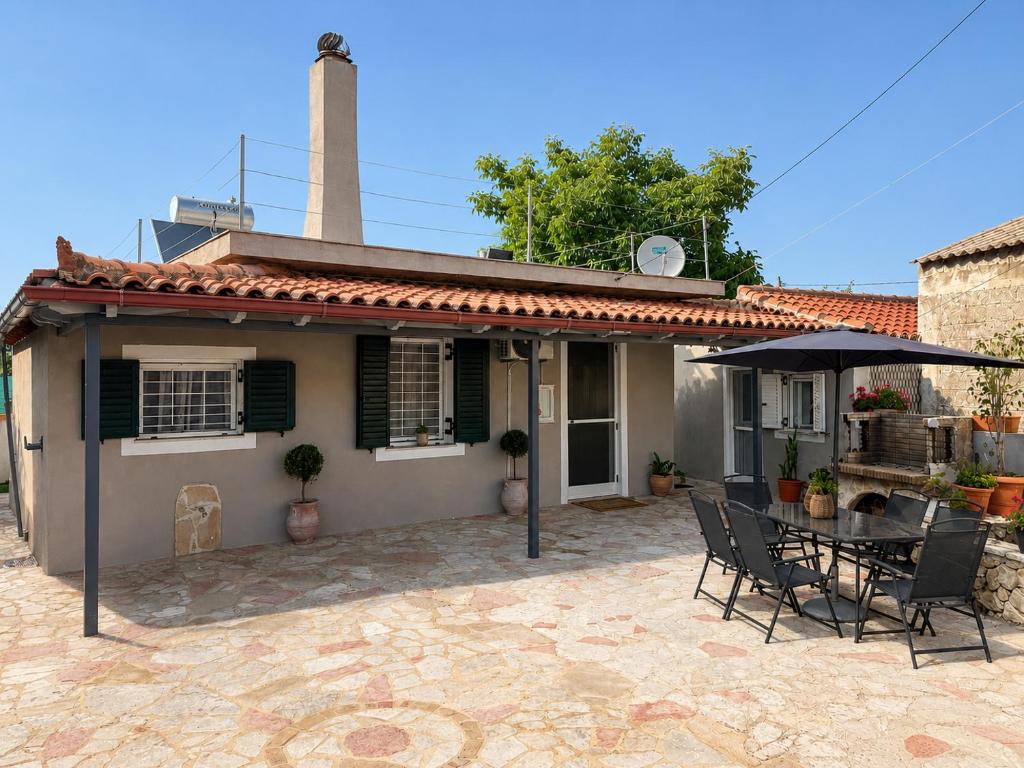 Ein Haus mit einer Terrasse, auf der ein Tisch und ein Sonnenschirm stehen. in der Unterkunft Selene House in Volímai