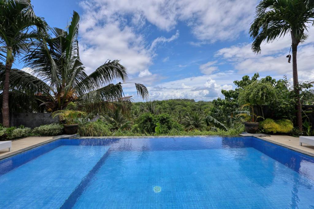 a large blue swimming pool with trees in the background at Kelingking Sunset Point Hotel in Nusa Penida
