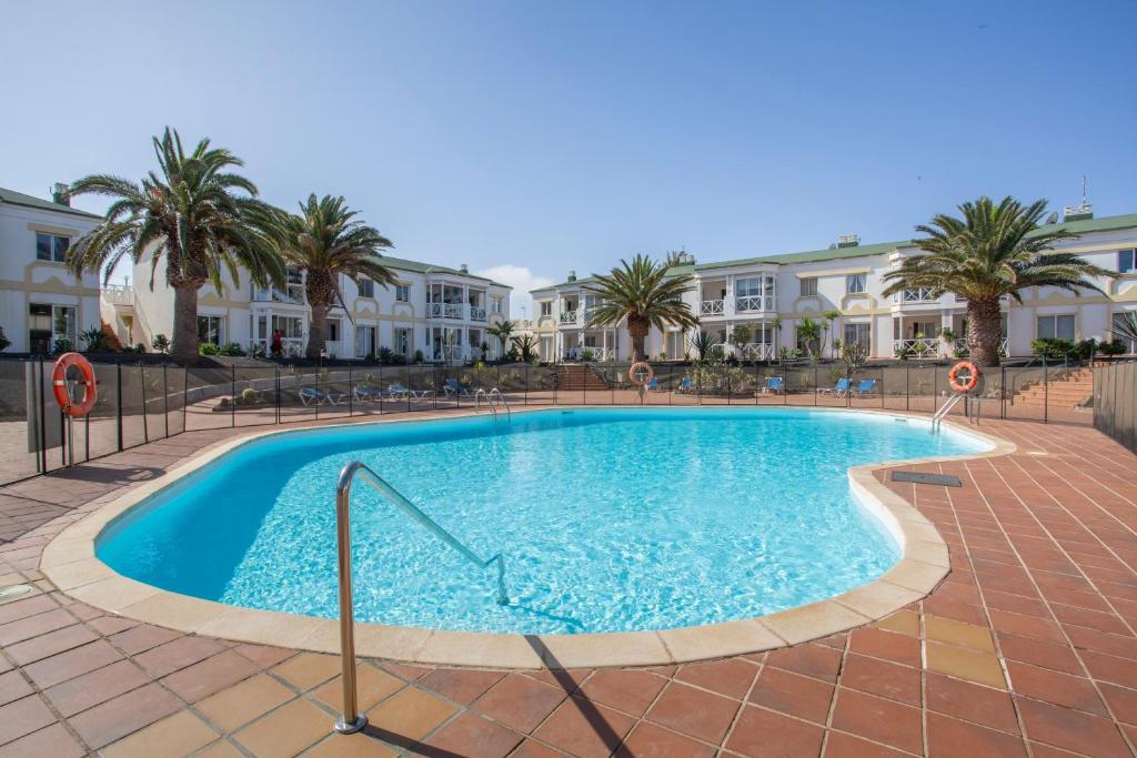 a pool with palm trees and buildings in the background at Piccola Oasi Corralejo in Corralejo