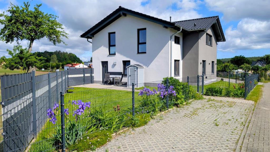 a white house with a fence and purple flowers at Ferienwohnung Am Kleinen Haff in Garz