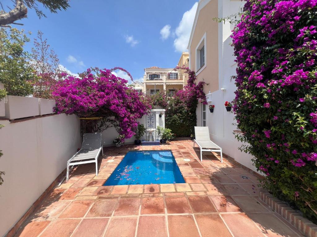 a backyard with a swimming pool with two chairs and purple flowers at VILLA AMIRA ,Marbella Estepona in Benahavís