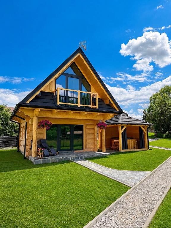 a log house with a deck on a green lawn at Domki góralskie Cisza Leśna in Czerwienne