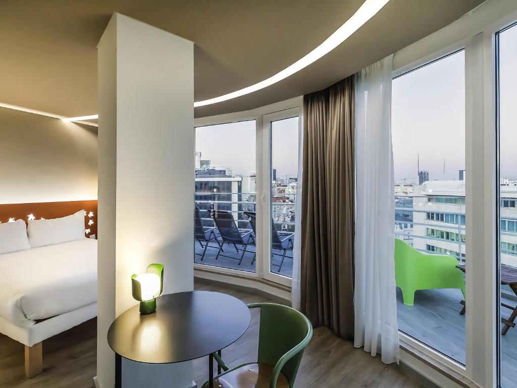 A bright room with a bed, round table, green chairs, and full-height doors onto an elevated balcony.