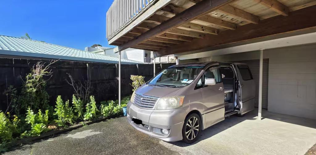 a small silver van parked next to a garage at Campvan Stay in Auckland