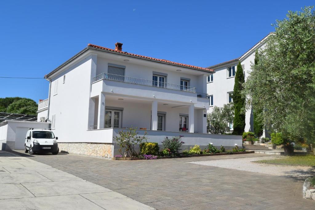 a white house with a car parked in front of it at Apartman Ivan in Malinska