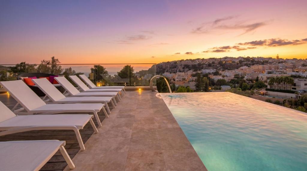 a pool with white lounge chairs and a sunset at Villa Ghea - Indoor Jacuzzi Pool, Sauna and Games Room in Mellieħa