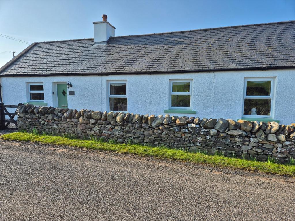 a white house with a stone wall in front of it at Beautiful 2-Bed semi rural cottage enclosed garden in Drummore