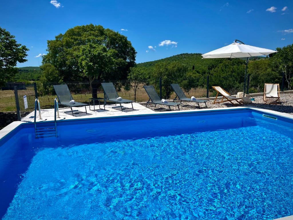a blue swimming pool with chairs and an umbrella at Peaceful New Country House with Saltwater Pool in Brgud
