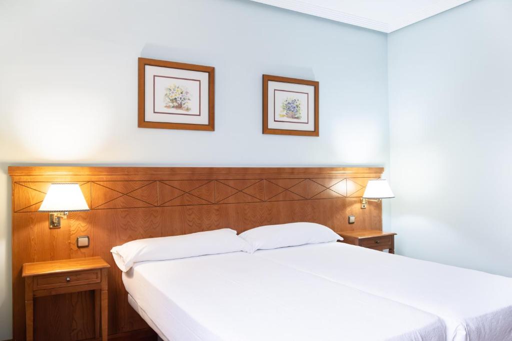 a bedroom with a white bed with two pictures on the wall at Checkin Basic León Norte in León