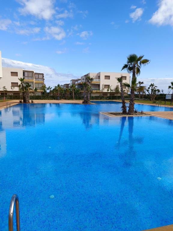 a large blue swimming pool with a palm tree at Odyssée Atlantique Blue beach - Sidi Rahal - famille seulement in Sidi Rahal