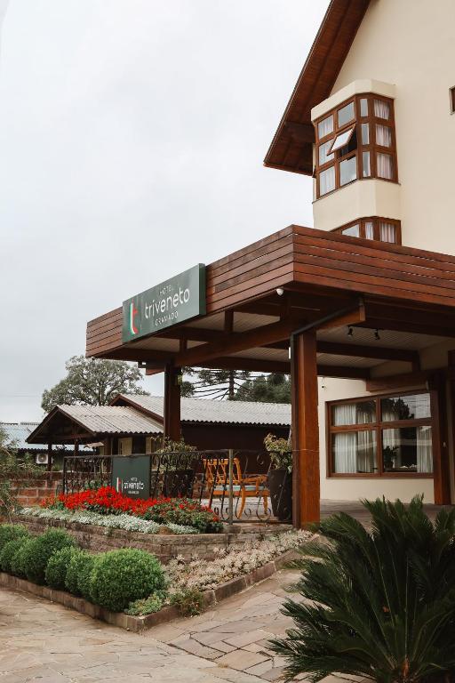 a building with a sign on it with chairs and flowers at Hotel Triveneto Gramado in Gramado