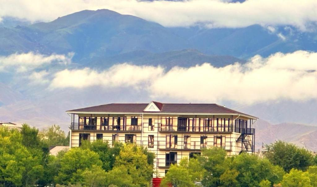 a large building with trees and mountains in the background at Ак-Кеме отель in Bosteri