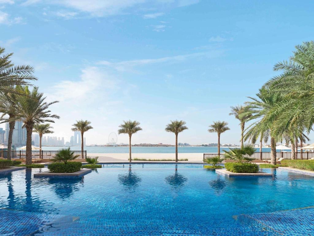 a swimming pool with palm trees and a body of water at Fairmont The Palm in Dubai