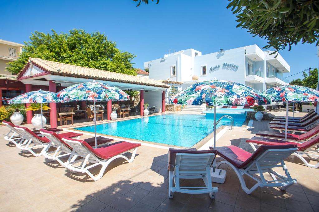 a pool with chairs and umbrellas next to a building at Perla Marina Hotel in Ialysos