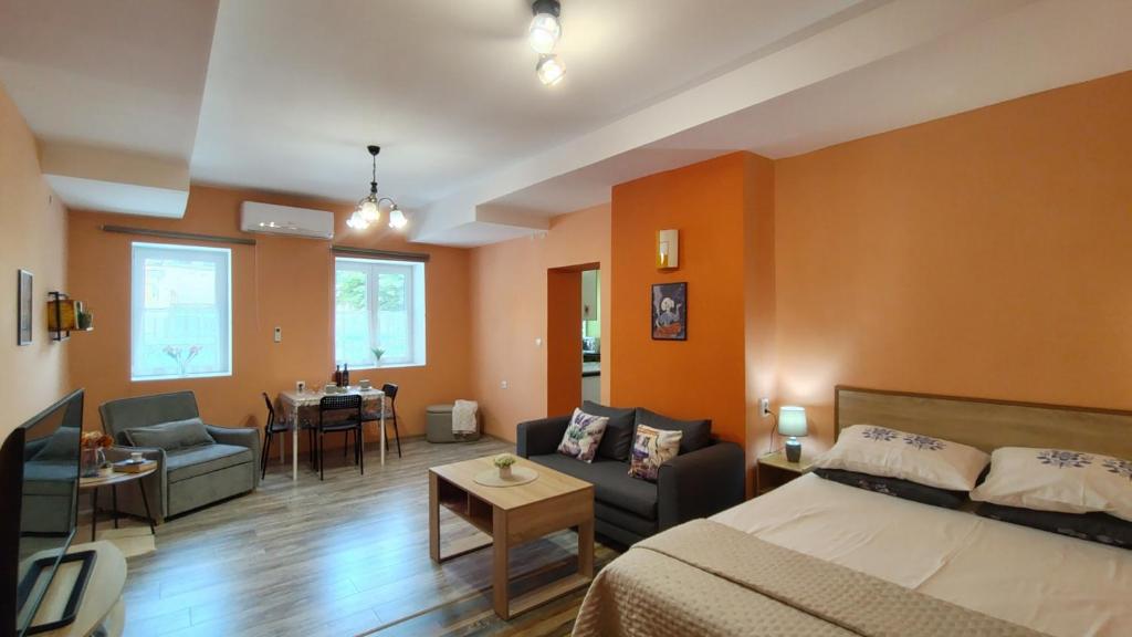 ein Schlafzimmer mit orangefarbenen Wänden und einem Bett und ein Wohnzimmer in der Unterkunft Уютно Централно Студио Враца in Vratsa
