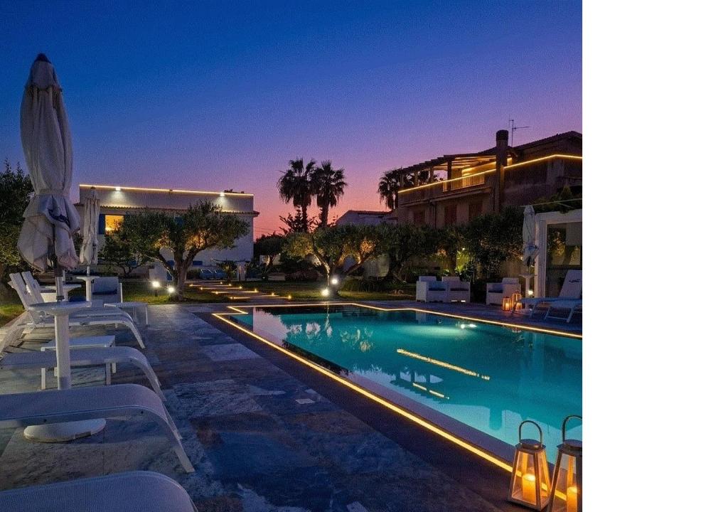 a swimming pool with white chairs and a building at Signorino Eco Resort & Spa in Marsala