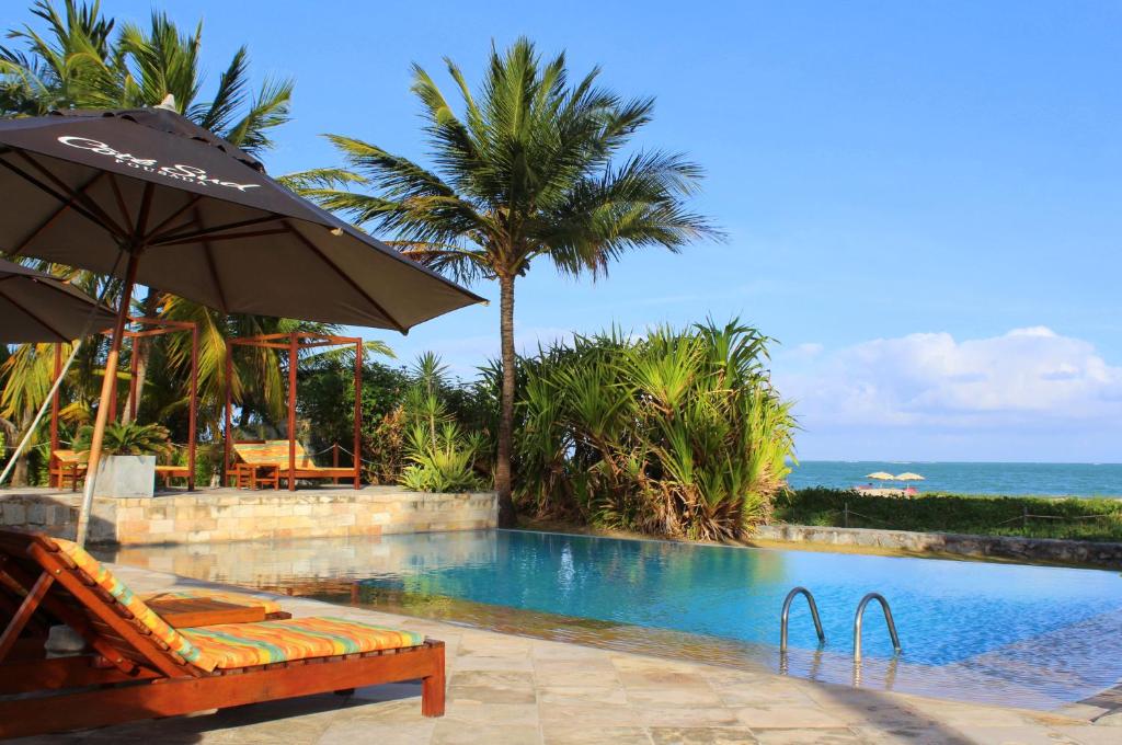 a swimming pool with an umbrella and a chair next to the ocean at Pousada Côté Sud in São Miguel dos Milagres