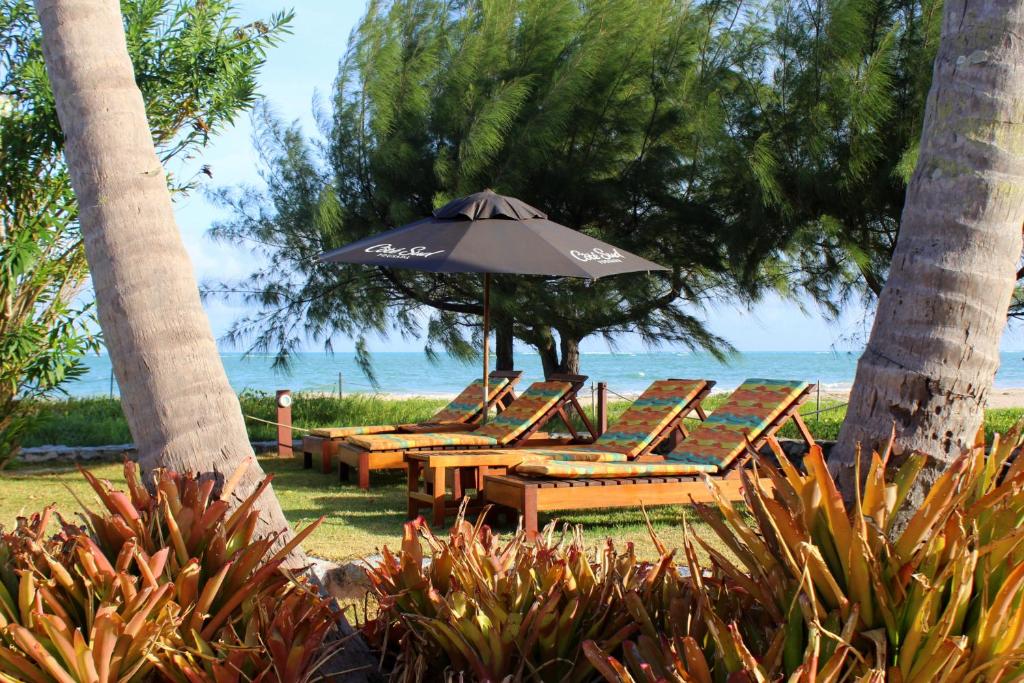 Un grupo de mesas y sillas con una sombrilla. en Villa Côté Sud Pousada De Charme, en São Miguel dos Milagres