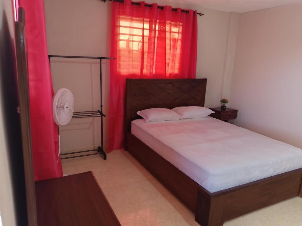 a bedroom with a bed and a window with red curtains at Complexe La Belle Rosie in Les Cayes
