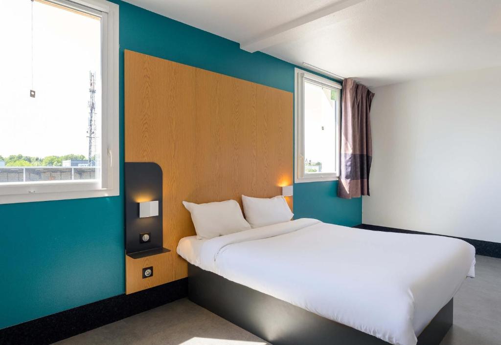 a bedroom with a bed and two windows at B&B HOTEL Lieusaint Carré Sénart in Lieusaint