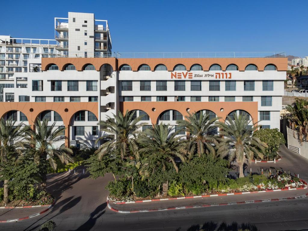 a large white building with palm trees in front of it at Neve Eilat Hotel By Atlas Hotels in Eilat