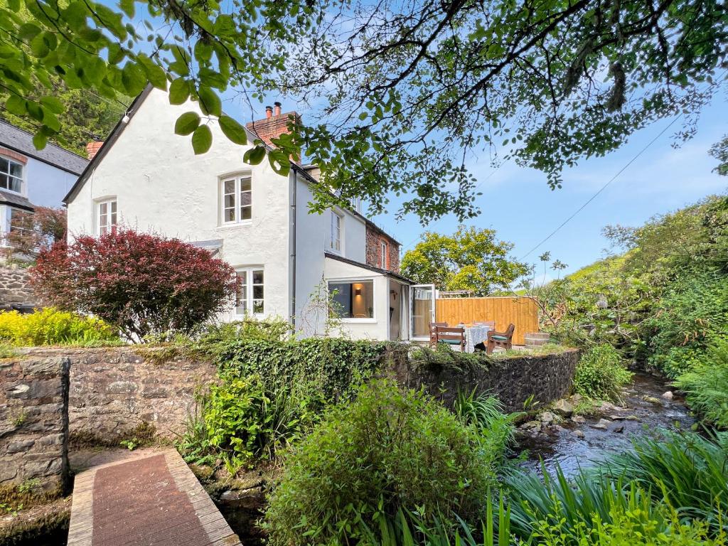 a white house with a stone wall next to a river at Glen Cottage Porlock in Porlock