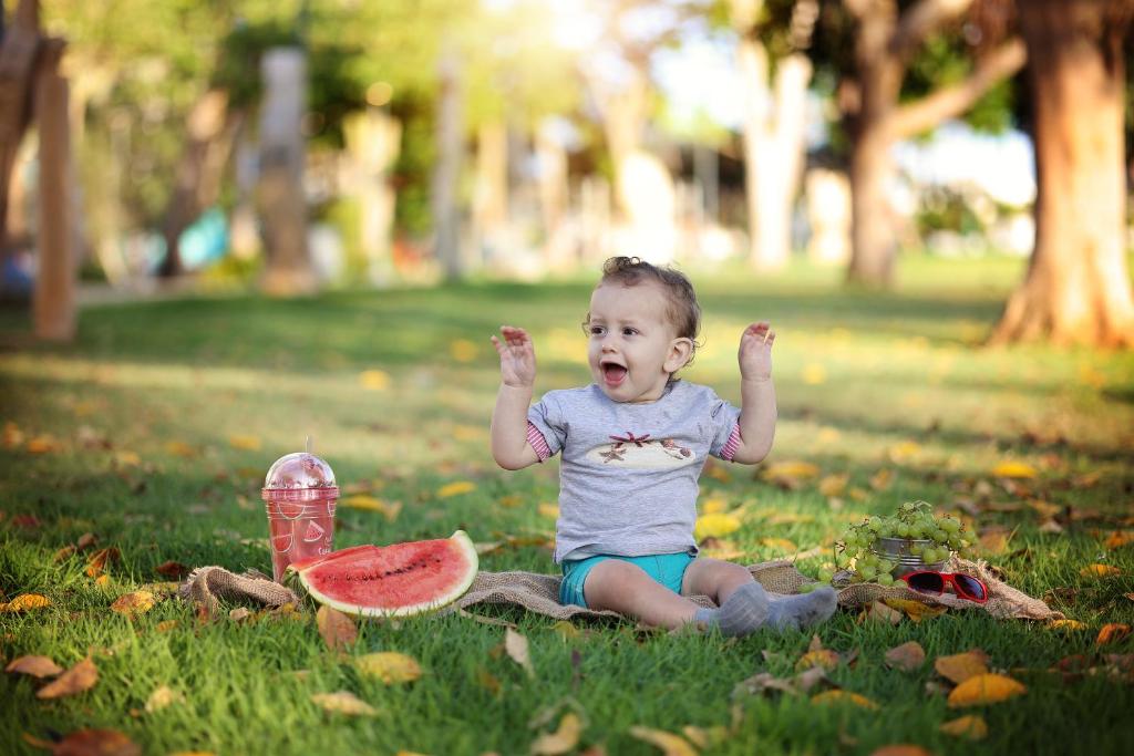 a baby sitting on the grass with a slice of watermelon at שובל shoval in Yavneʼel