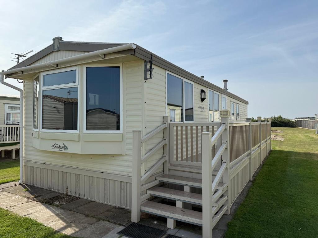 a white tiny house with a porch and stairs at Bell Bank C8 - pet friendly, bed linen, close to bars and shops - Meadow Lakes Caravan & Lodge Hire in Chapel Saint Leonards