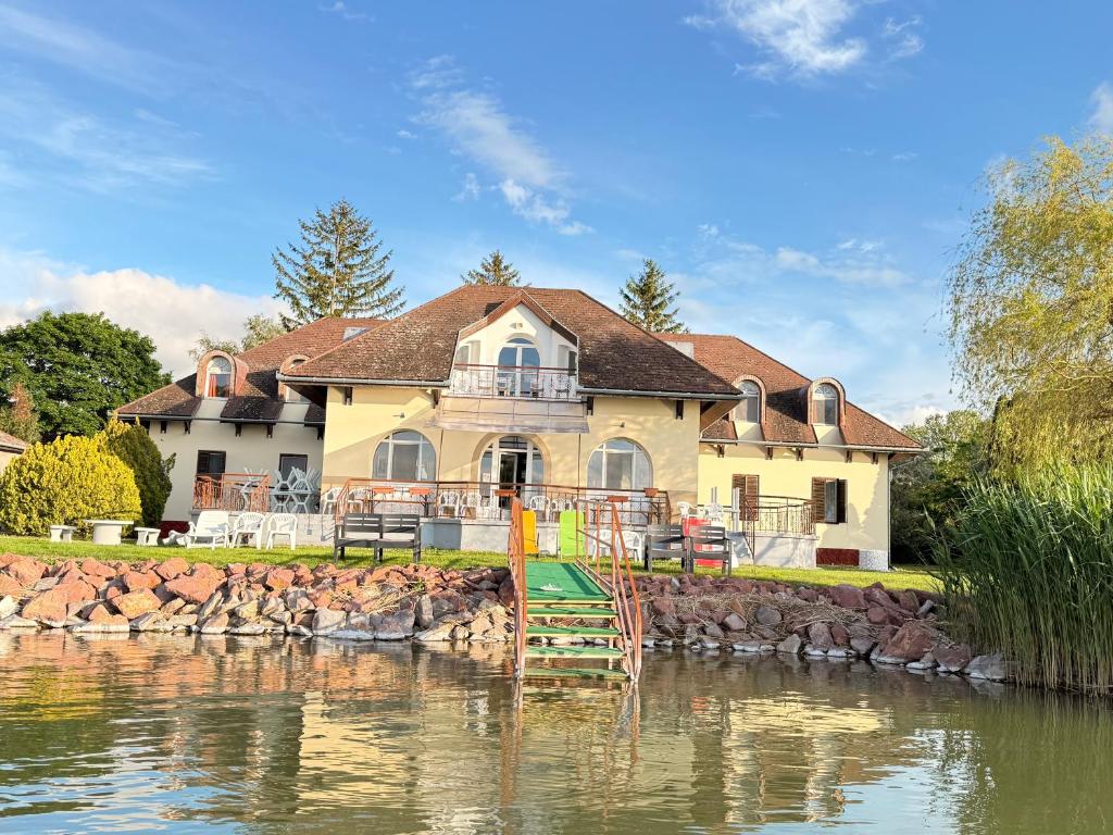 a large yellow house next to a body of water at Aranyhídszálló in Balatonboglár