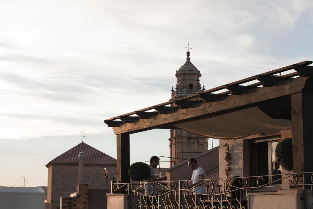 two people sitting on a balcony of a building with a clock tower at La Casa dels Abeuradors in Gandesa