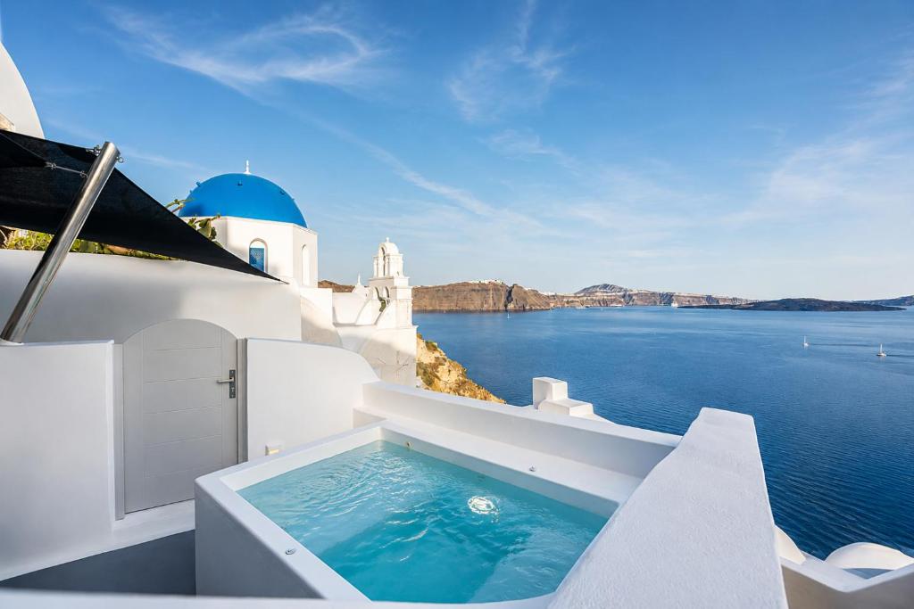a swimming pool on the side of a house with the ocean at Three Domes Oia - an Iconic Collection in Oia