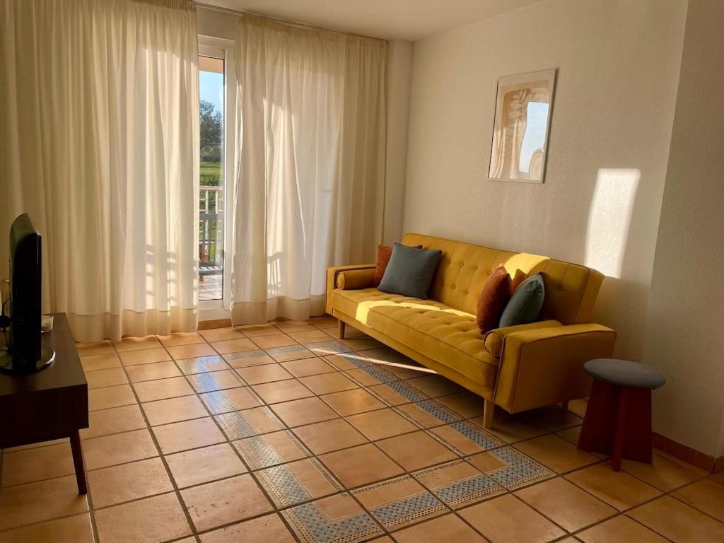 a living room with a yellow couch in front of a window at Golf Paradise in Sant Jordi