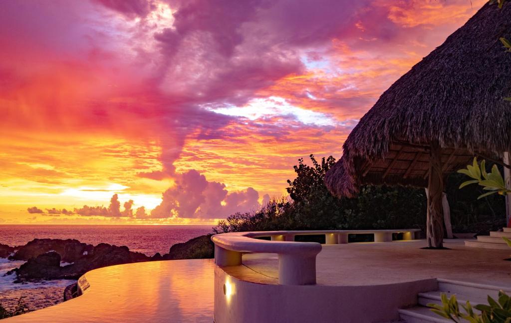 a sunset at a beach with a thatch roof at Casa Papelillo on Costa Careyes in Chamela