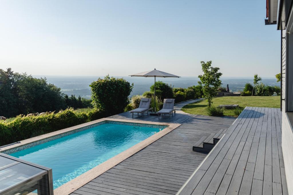 a pool with two chairs and an umbrella on a wooden deck at PanoramaLodge Samerberg in Samerberg