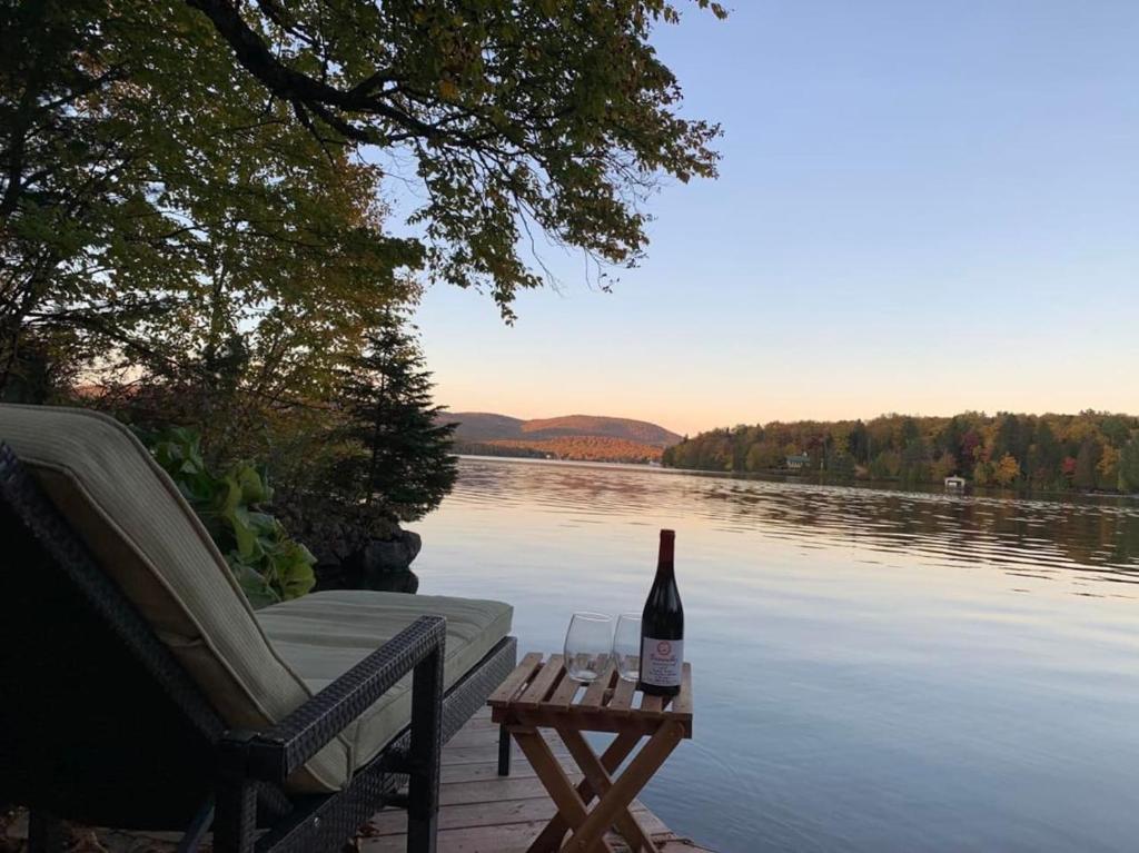 a bottle of wine on a picnic table next to a lake at Lakefront Chalet Hot Tub & Fire Pit Sleeps 6 in Saint-Raymond