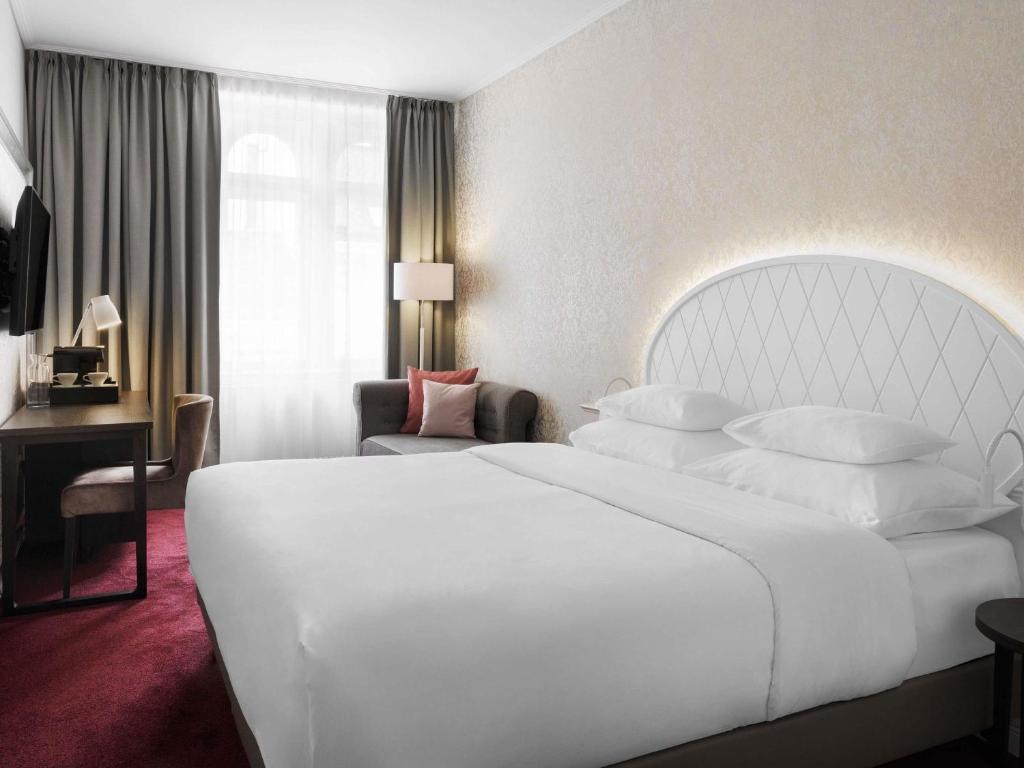 a bedroom with a large white bed and a desk at Hotel Rathauspark Wien - Handwritten Collection in Vienna