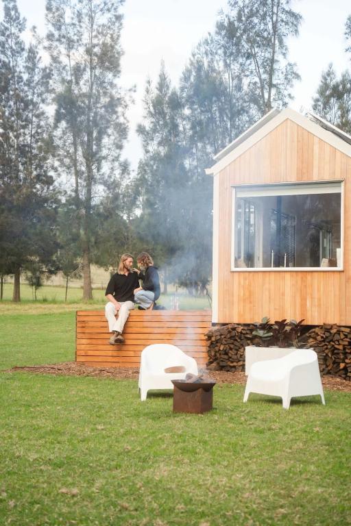 two people sitting on a wooden bench next to a building at The Antidote Luxe Off-Grid Tiny Home Escape on Private Farm Stay in Farmeadow