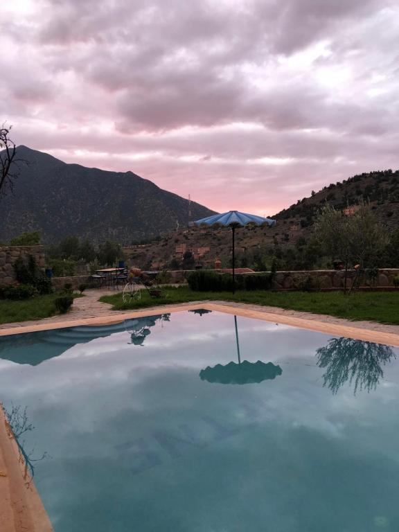 a pool of blue water with an umbrella and mountains at Auberge soultana in Agouni