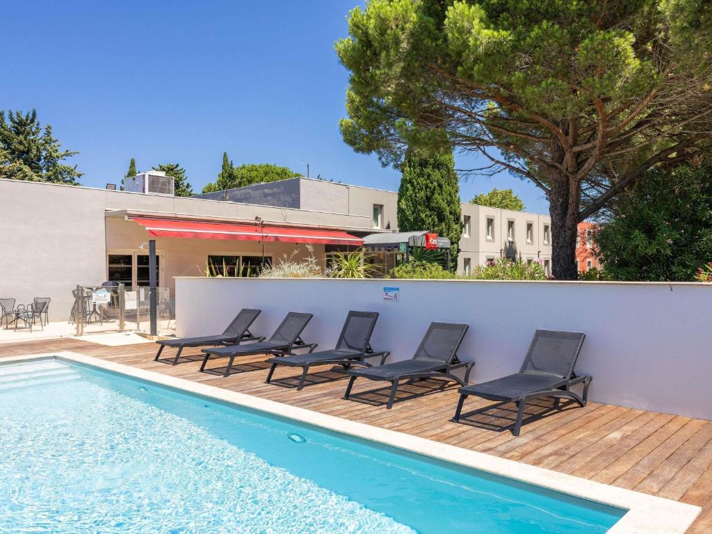 a swimming pool with chairs next to a white wall at ibis Carcassonne Est la Cité in Carcassonne