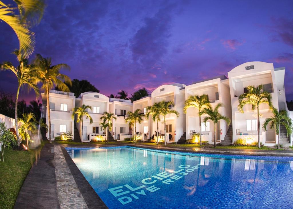 a swimming pool in front of a building with palm trees at El Cielo Resort in Dauin
