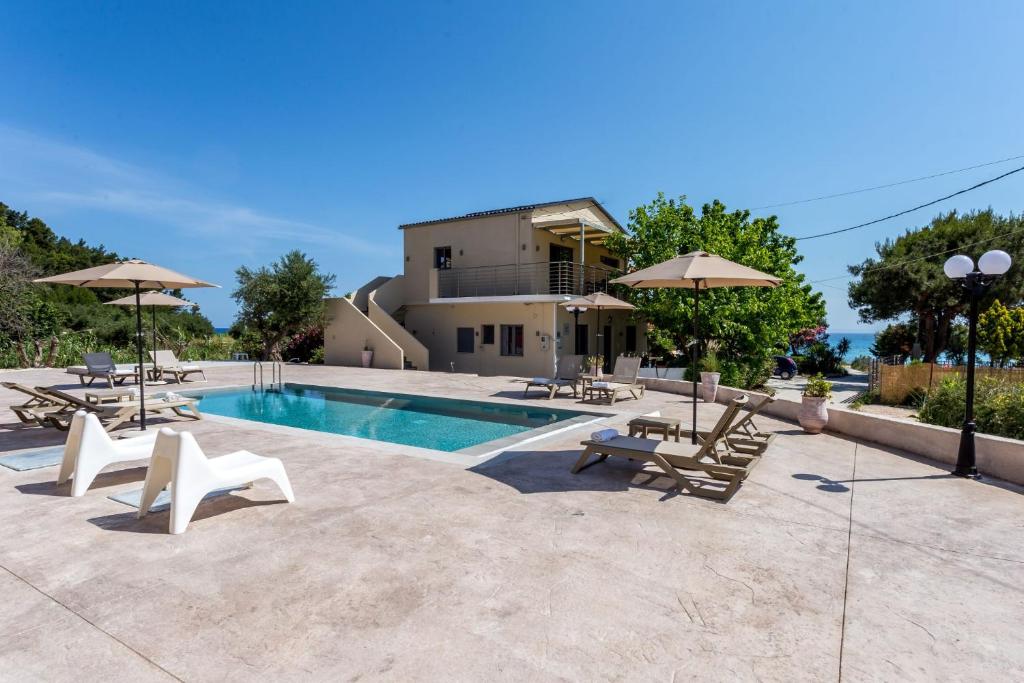 a swimming pool with chairs and umbrellas in front of a house at Casa Di Mare - Studios and Apartments with pool on the beach, by ZanteWize in Vasilikos
