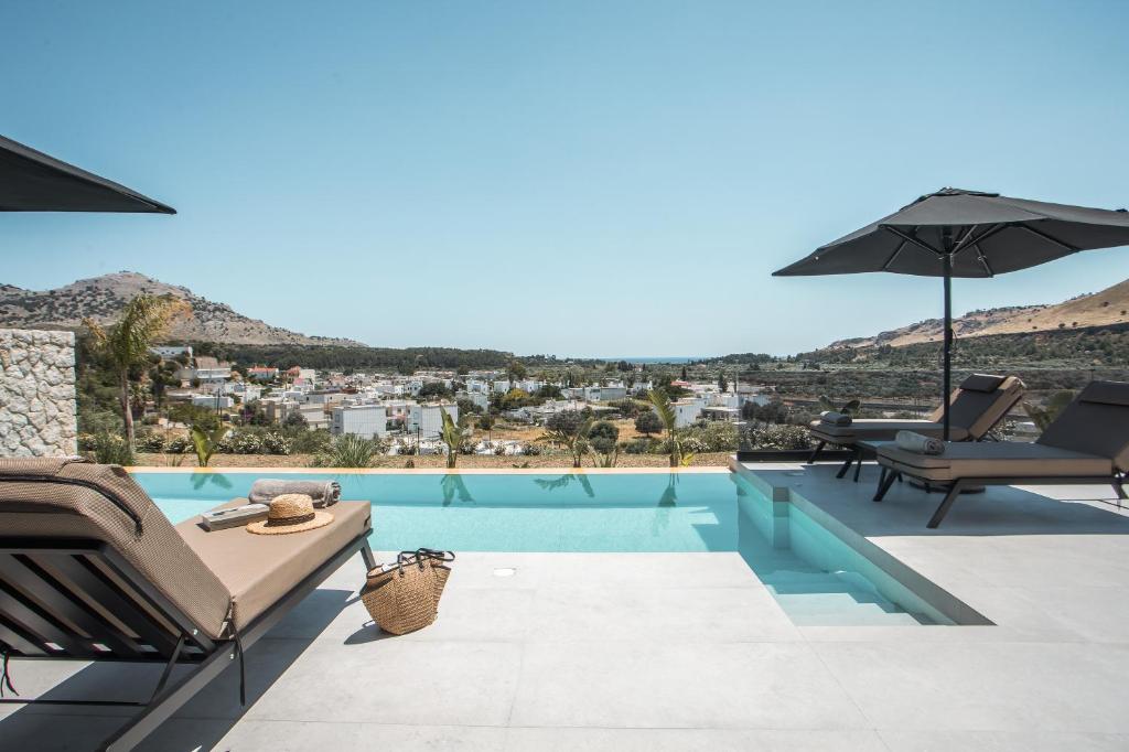 a villa with a swimming pool with chairs and an umbrella at Celeste Luxury Villas in Lartos