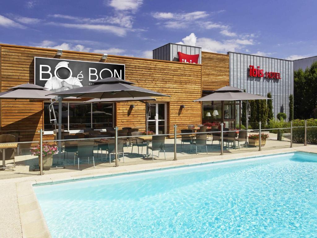 a restaurant with a swimming pool in front of a building at Ibis Roanne Le Coteau Hotel Restaurant in Le Coteau